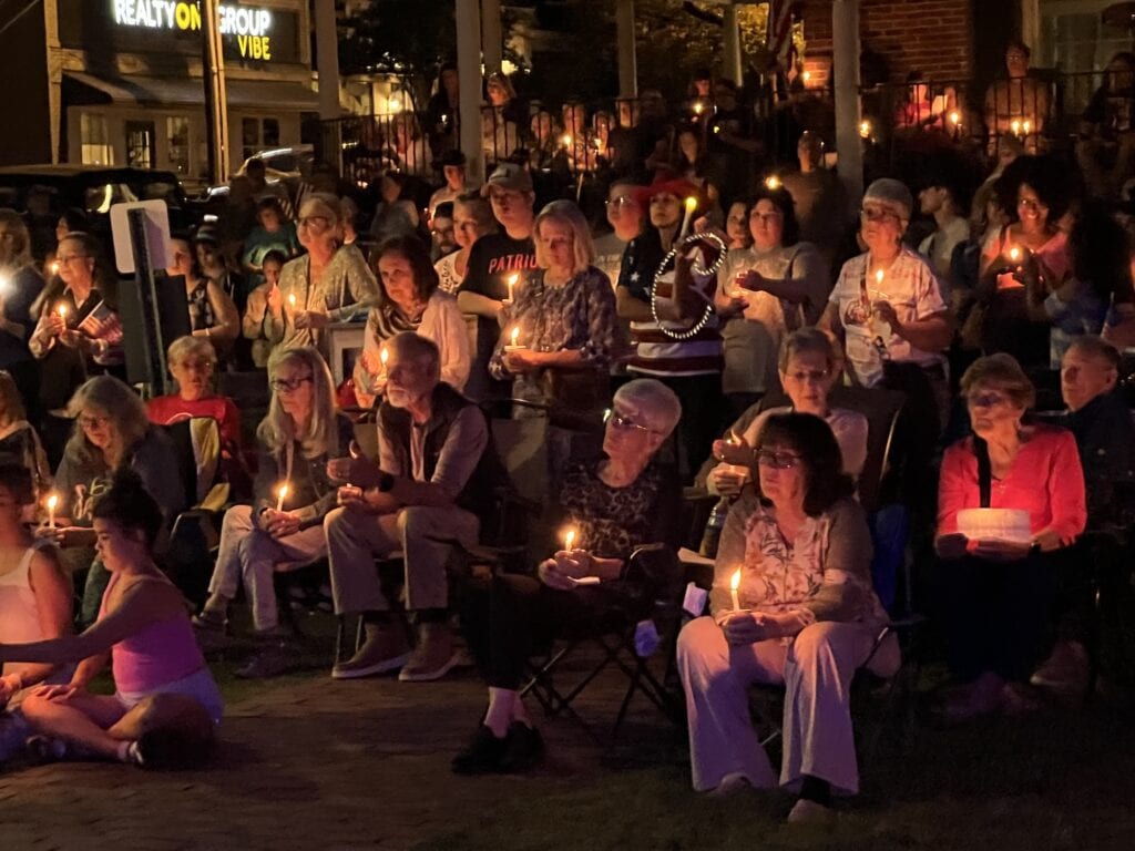 People gathered outdoors holding candles in prayer for America.