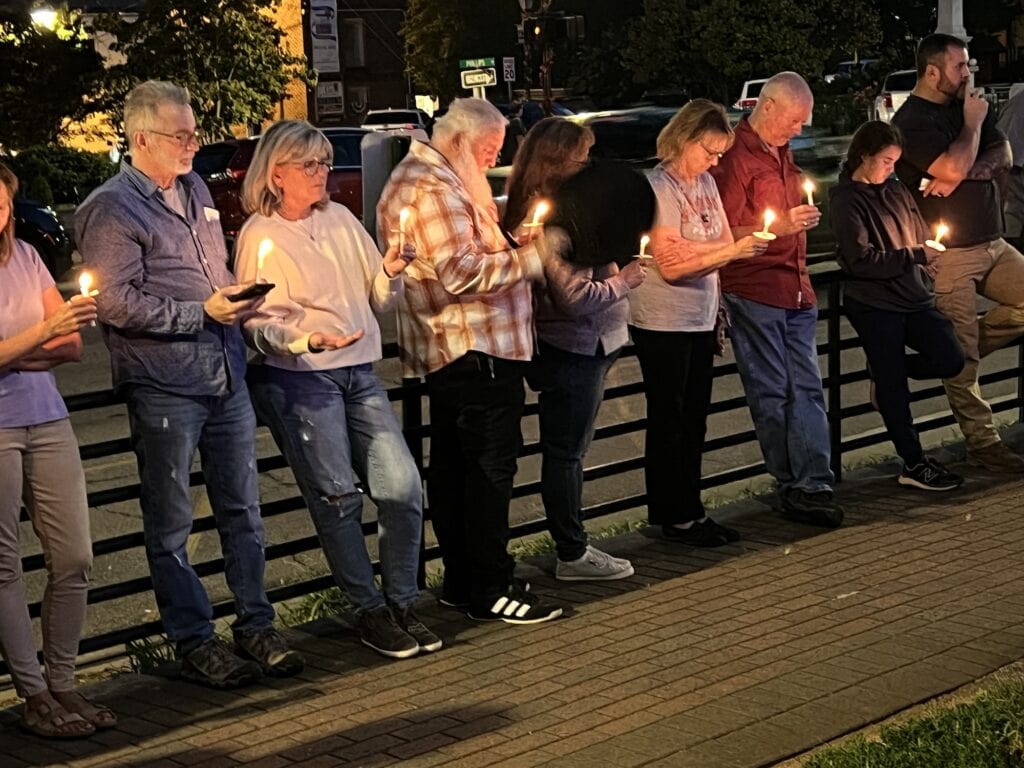 People holding candles during prayer for America at dusk.