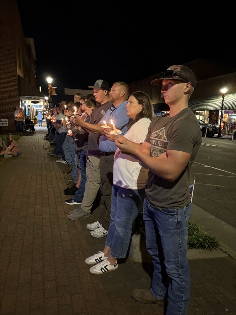 Group of people praying with candles during night in a public space.