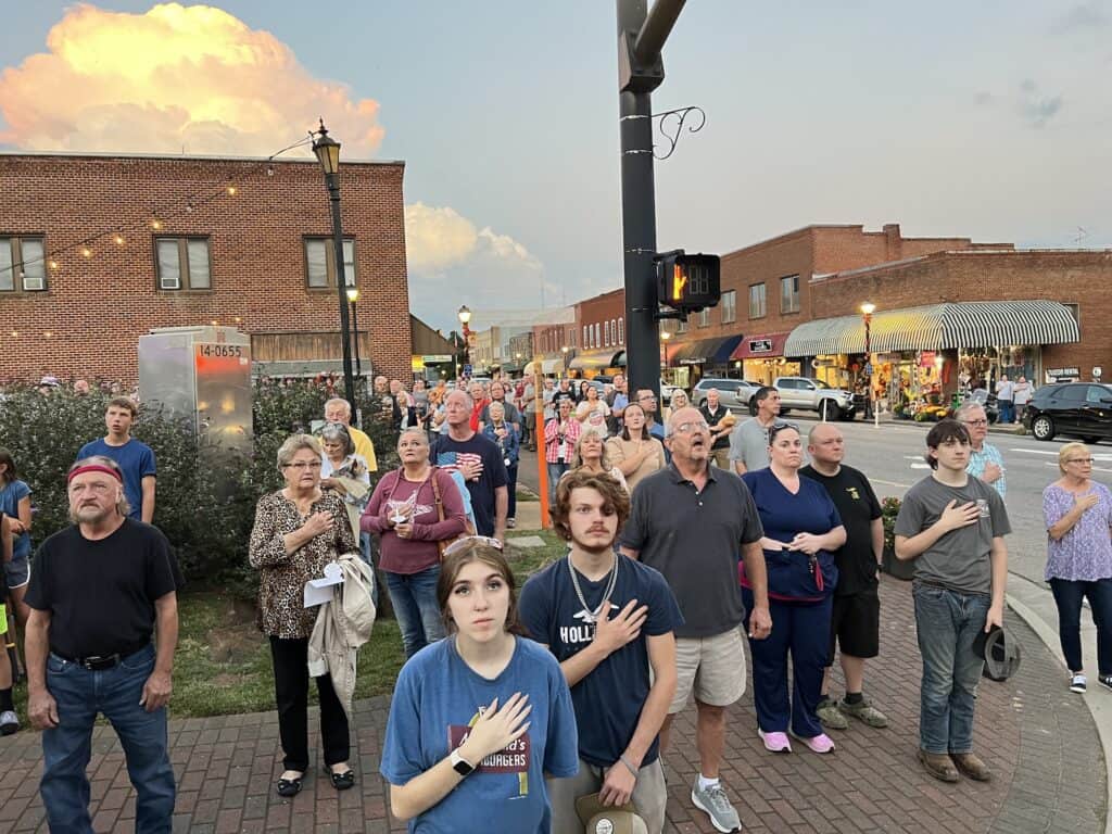 Group of diverse people praying together outdoors in a small town setting.
