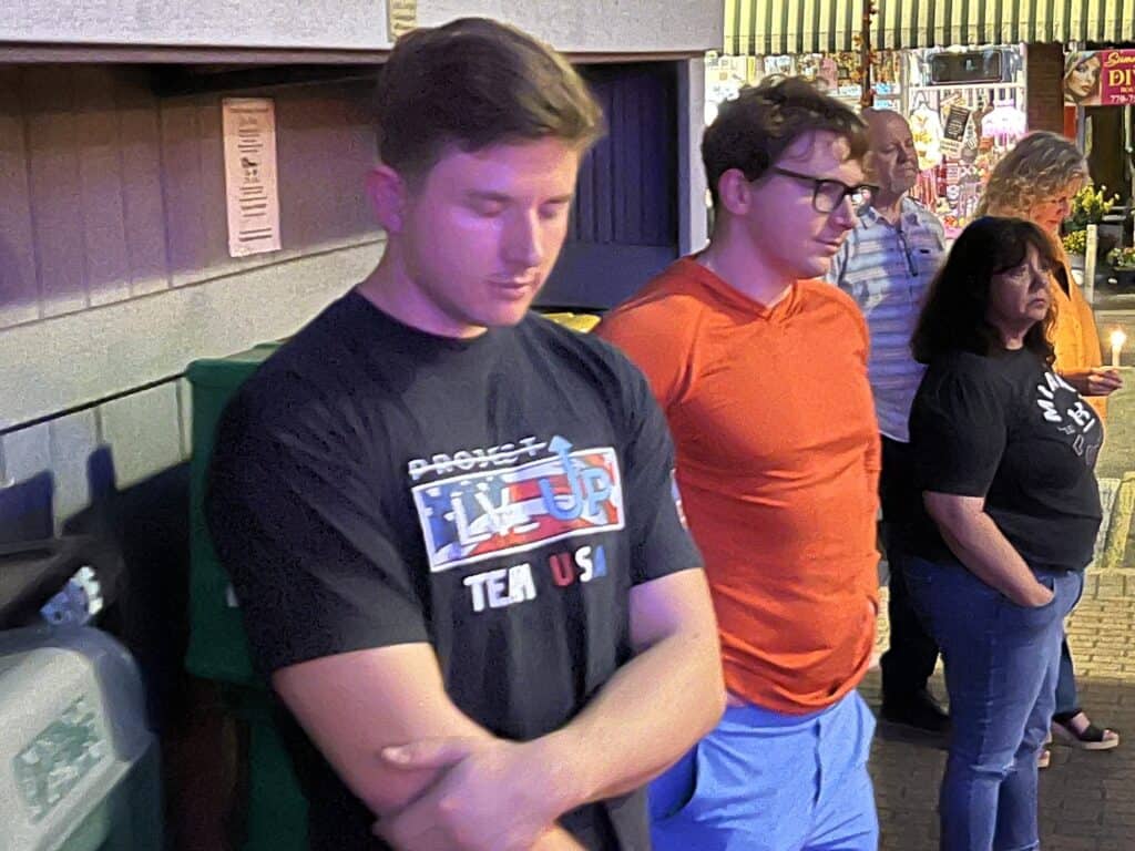 Group of people praying outdoors with patriotic theme in the background.