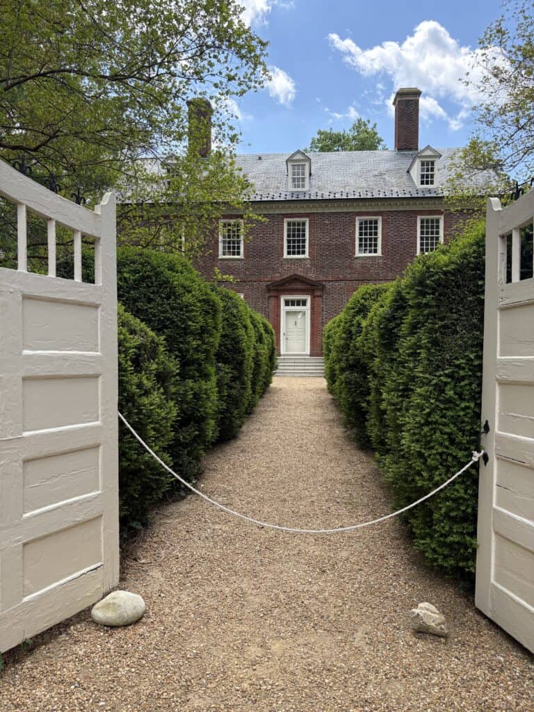 American colonial house surrounded by lush greenery and a gravel pathway leading to the entrance.