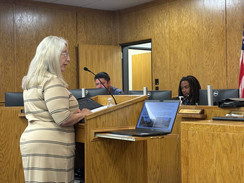 Woman speaking at a Macon Sense community meeting in a wood-paneled room.