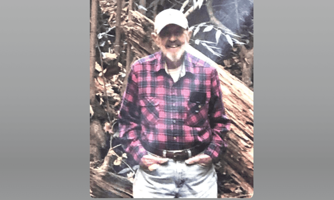 Ronald Ellsworth Reeme outdoors in a forest setting, wearing a plaid shirt and cap.