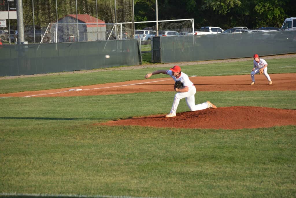 Youth baseball game with players pitching and fielding on a sunny day.