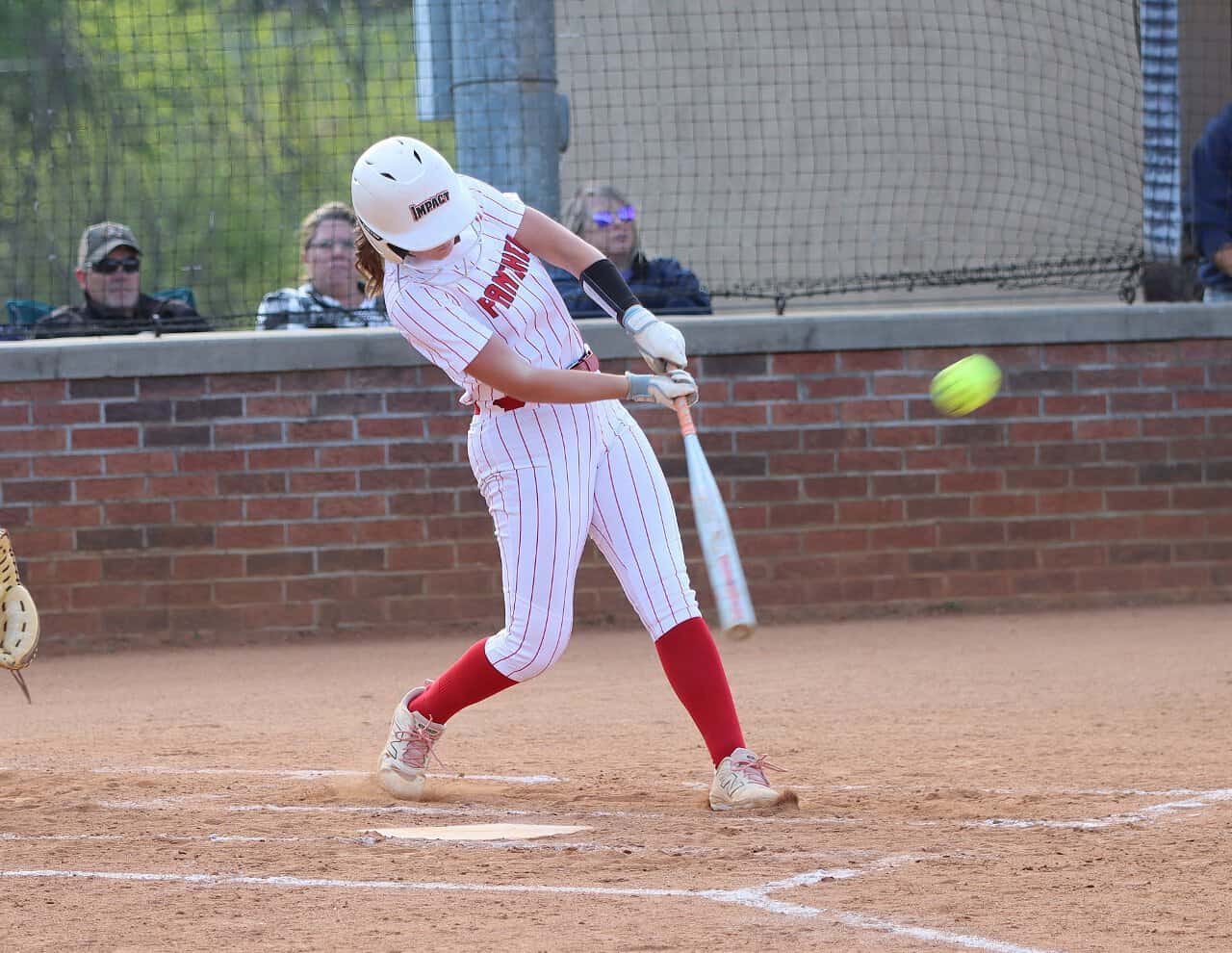 Female softball player swinging at a pitch during a game.