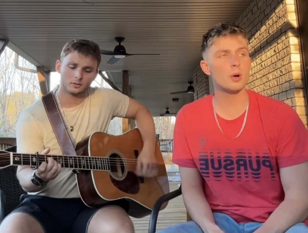 Young men performing guitar and singing outdoors.