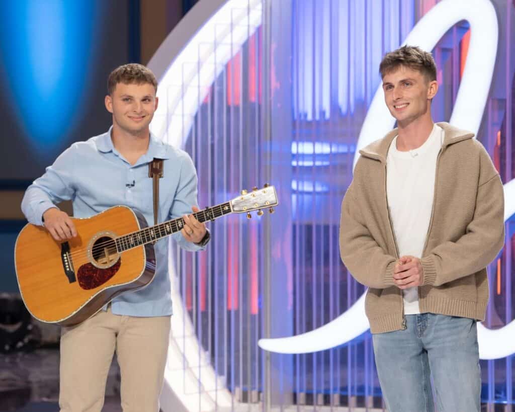 Young male singer with guitar on American Idol stage.