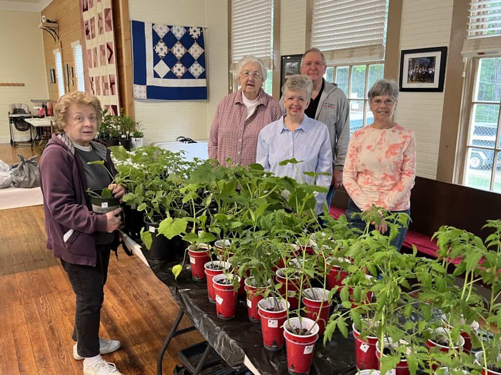 Elderly women and a man enjoy a gardening activity with potted plants indoors.