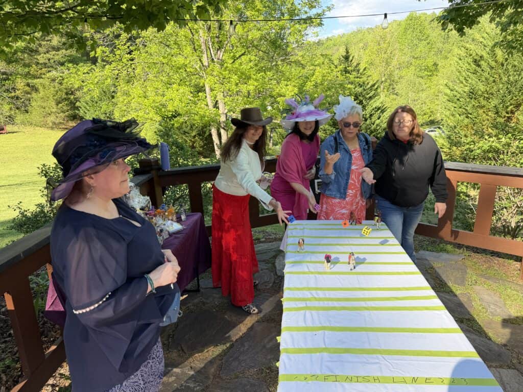 Women in stylish hats and dresses enjoying a game outdoors on a sunny deck.