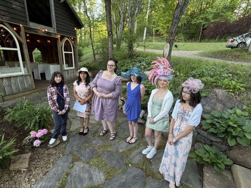 Women in stylish hats attending outdoor garden event in lush green setting.