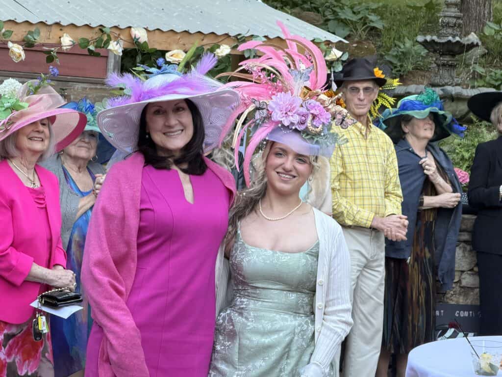 Women wearing stylish, vibrant hats and dresses at outdoor social gathering.