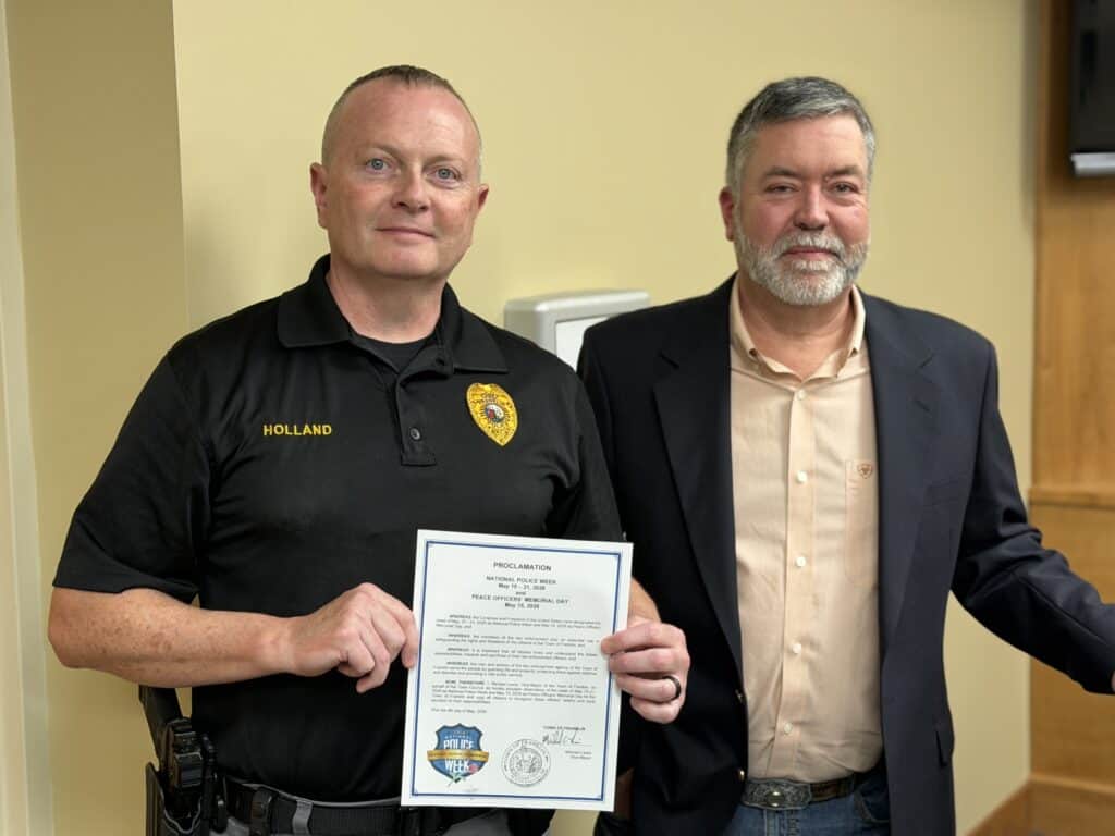 Police officer holding a certificate of recognition with a colleague.