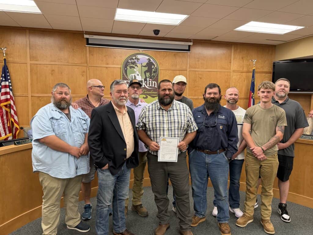 Group of diverse men standing in a council room with Macon County emblem.