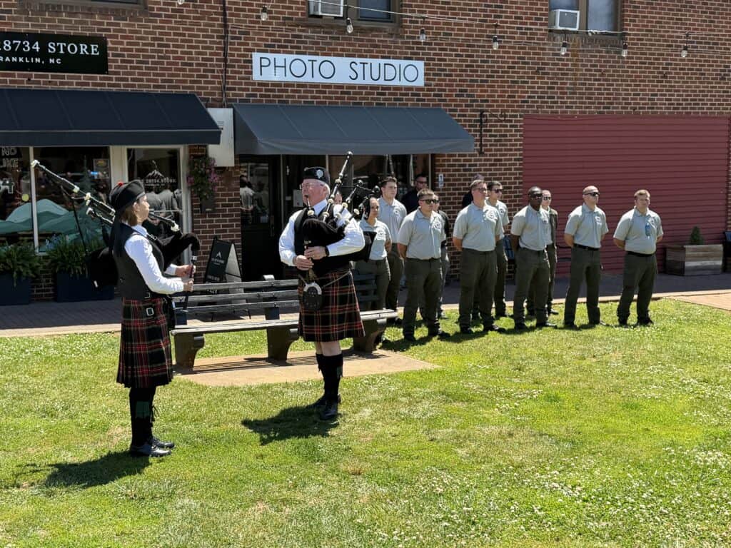 Bagpipers in kilts playing music outside a photo studio building.