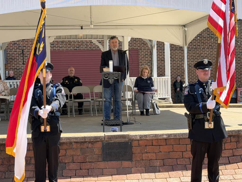 Memorial ceremony featuring flag bearers and a speaker at Macon Sense event.