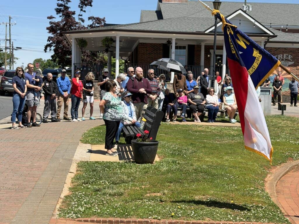Community memorial gathering at Macon Sense with people paying respects outdoors.