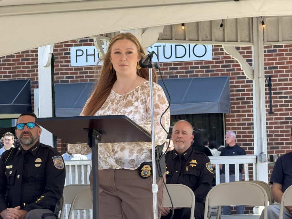 Woman speaking at outdoor event with police officers present.