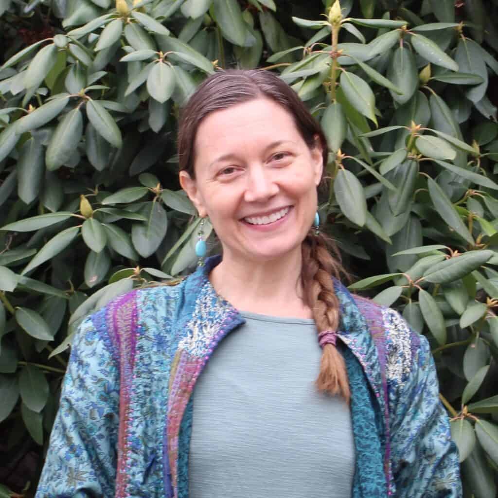 Woman smiling outdoors with lush green foliage background, representing leadership.