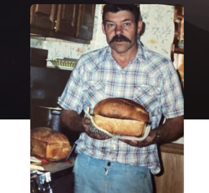 Man holding a large sandwich in a home kitchen setting.