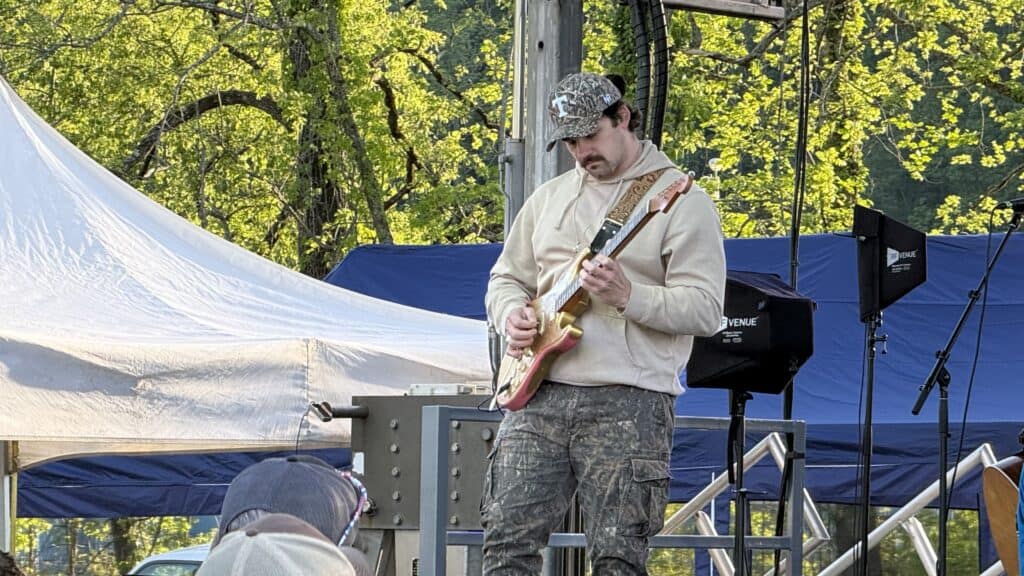 Musician performing at spring festival with trees and tents in background.