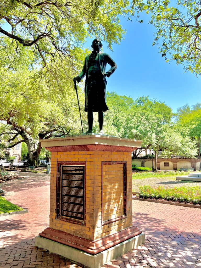 Historic Macon Sense statue in a lush park with trees and brick pathways.