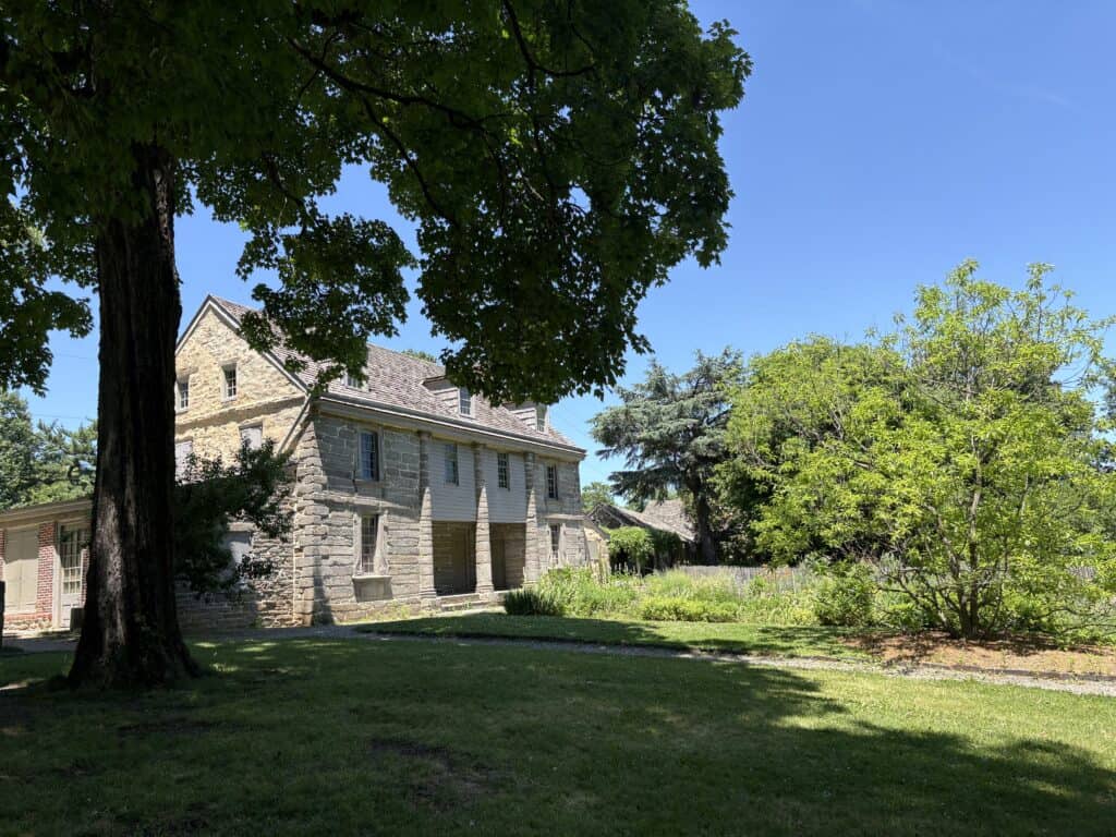 Stone house surrounded by trees and garden under blue sky.
