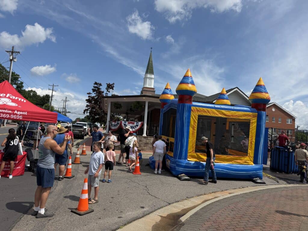 People enjoying a community event with inflatable castle and tents.