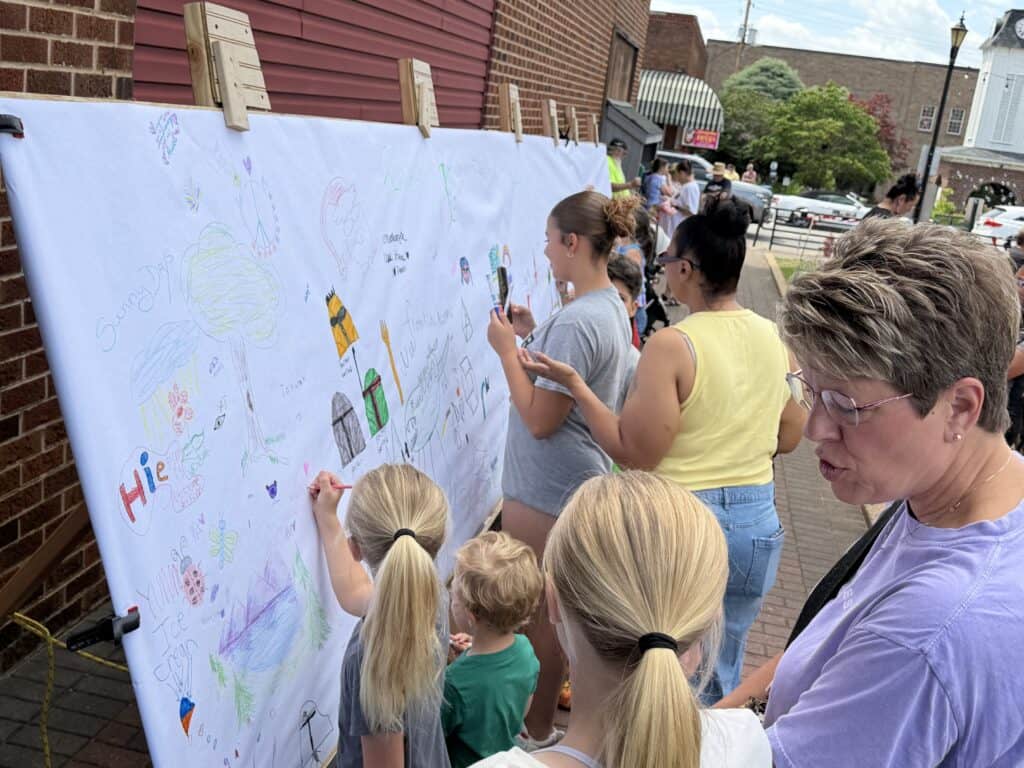People of all ages drawing and writing on a large community art wall.