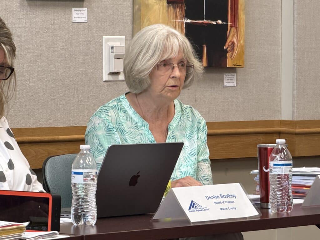 Elderly woman with gray hair using a laptop at an art exhibition.