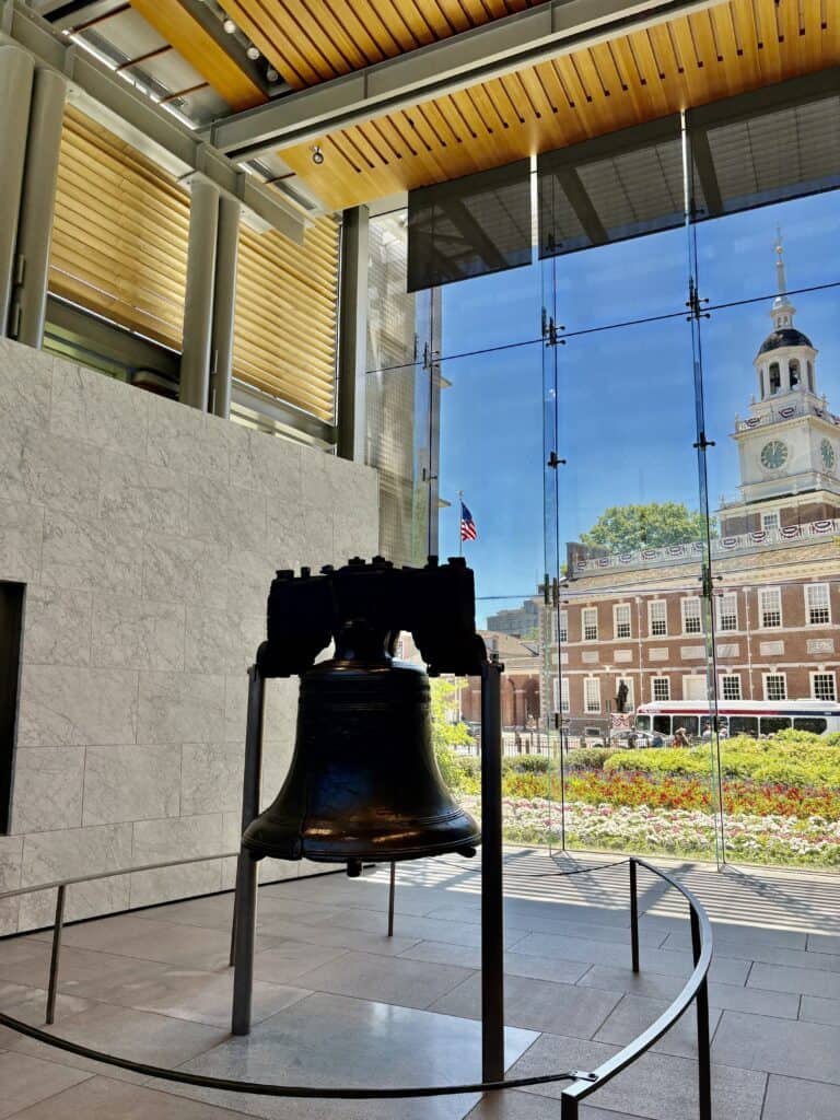 Close-up of the Liberty Bell inside Independence Hall with a view of Independence Hall outside.