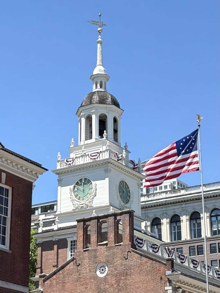 Iconic clock tower at Independence Hall with American flag and blue sky.