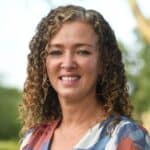 Woman with curly hair smiling outdoors, new town manager appointment.