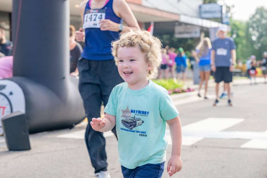 Young child smiling and running during a community race event.
