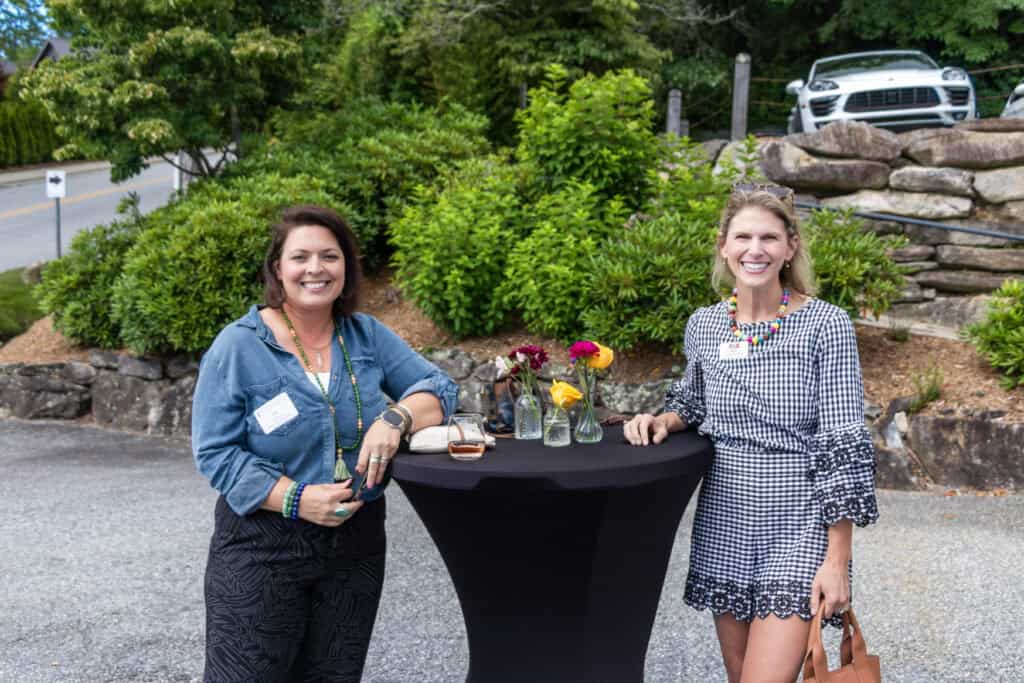 Two women networking at Highlands Chamber outdoor event with drinks and flowers.