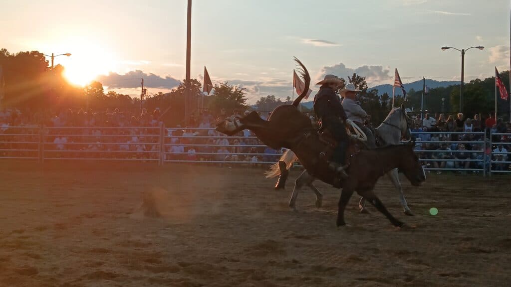 Rodeo cowboy on bucking horse at sunset during a rodeo event.