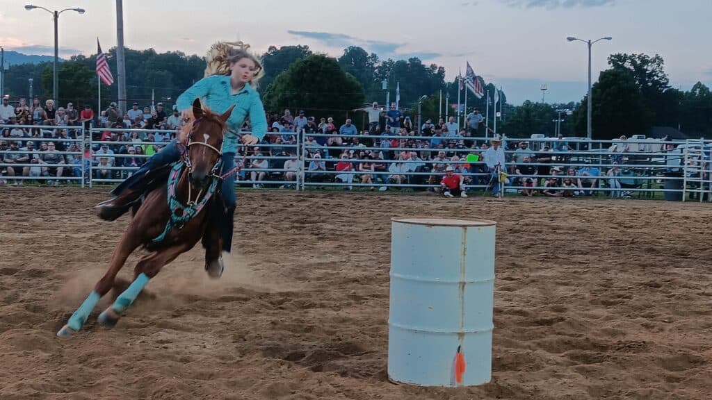Girl riding a barrel at a rodeo event with a crowd in the background.