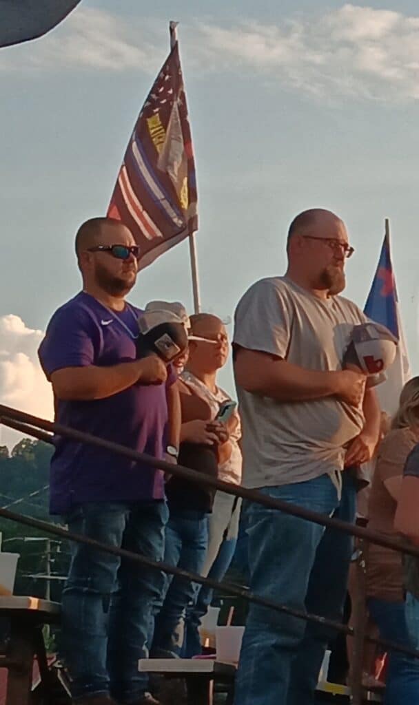 Fans holding flags and helmets at a rodeo event in the outdoors.