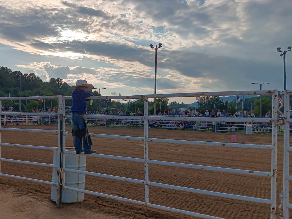 Rodeo arena with a cowboy leaning on the fence at sunset.