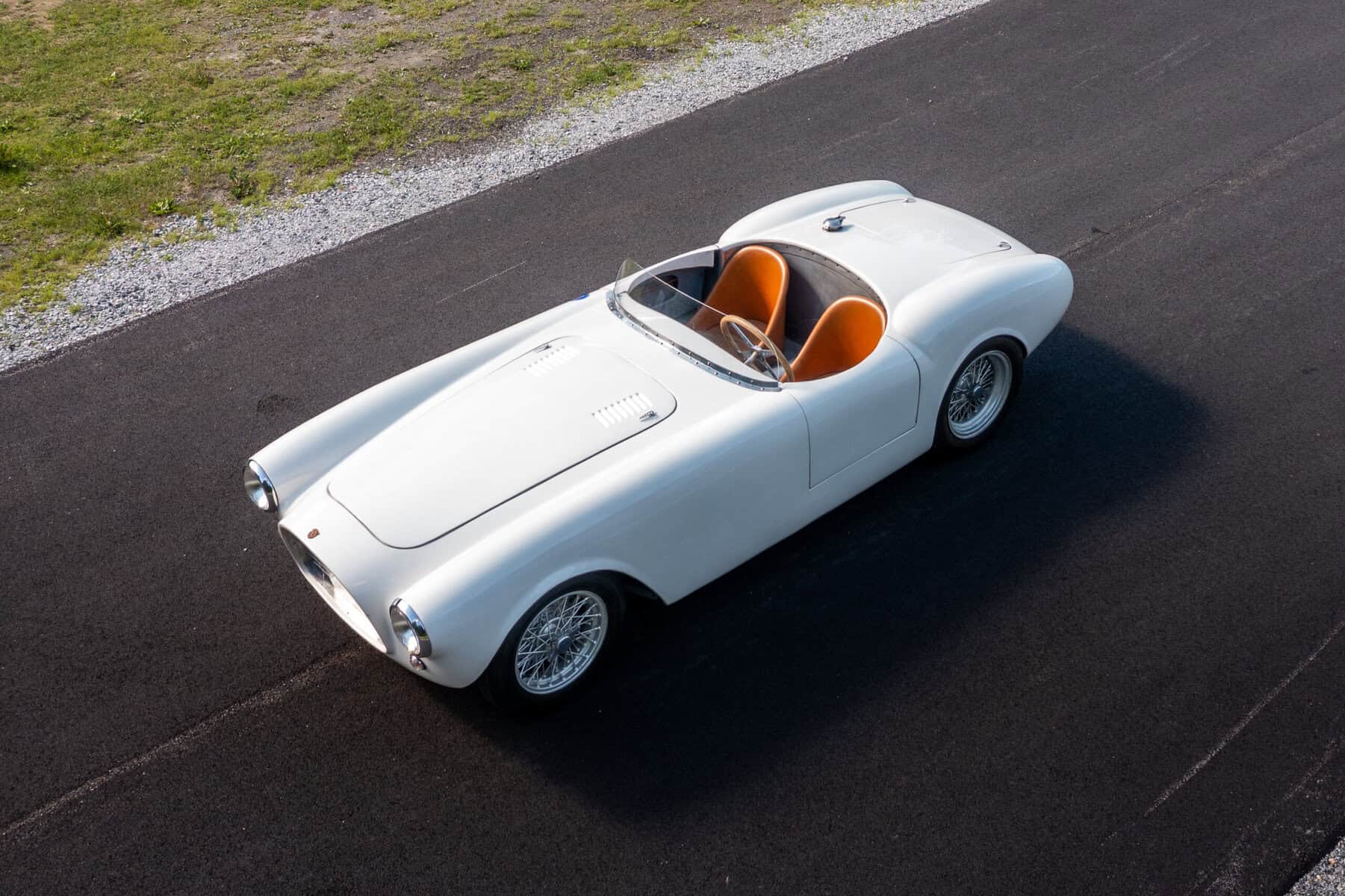Elegant white vintage sports car with orange interior on asphalt road.