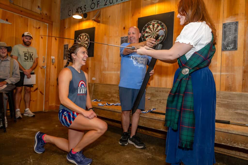 Woman in tartan skirt playing darts with a woman kneeling in front.
