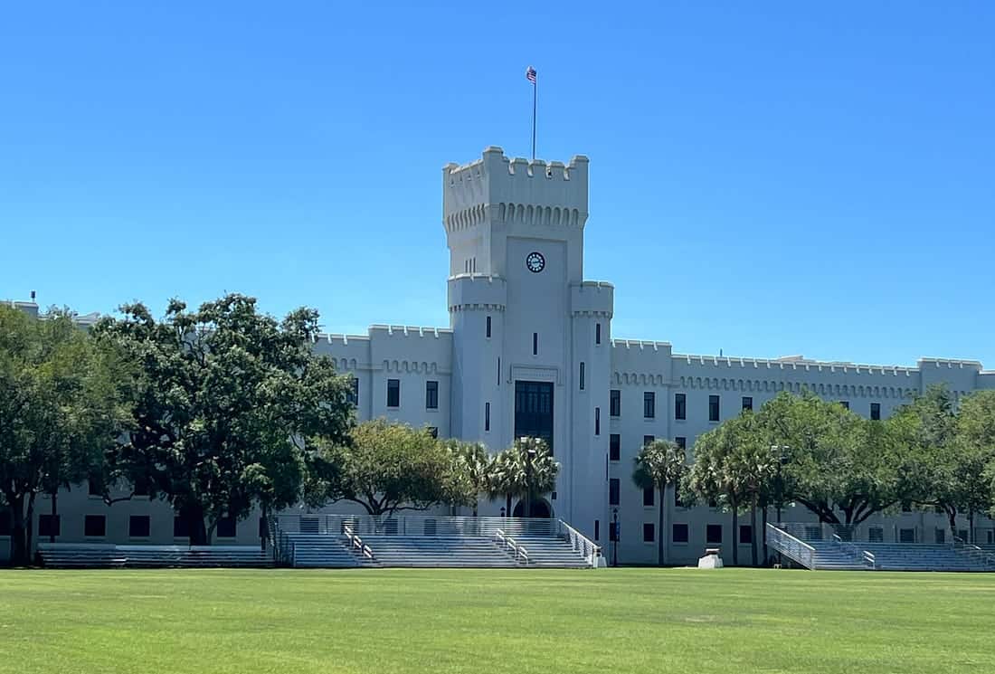 White castle-like military academy with a clock tower and lush green lawn.