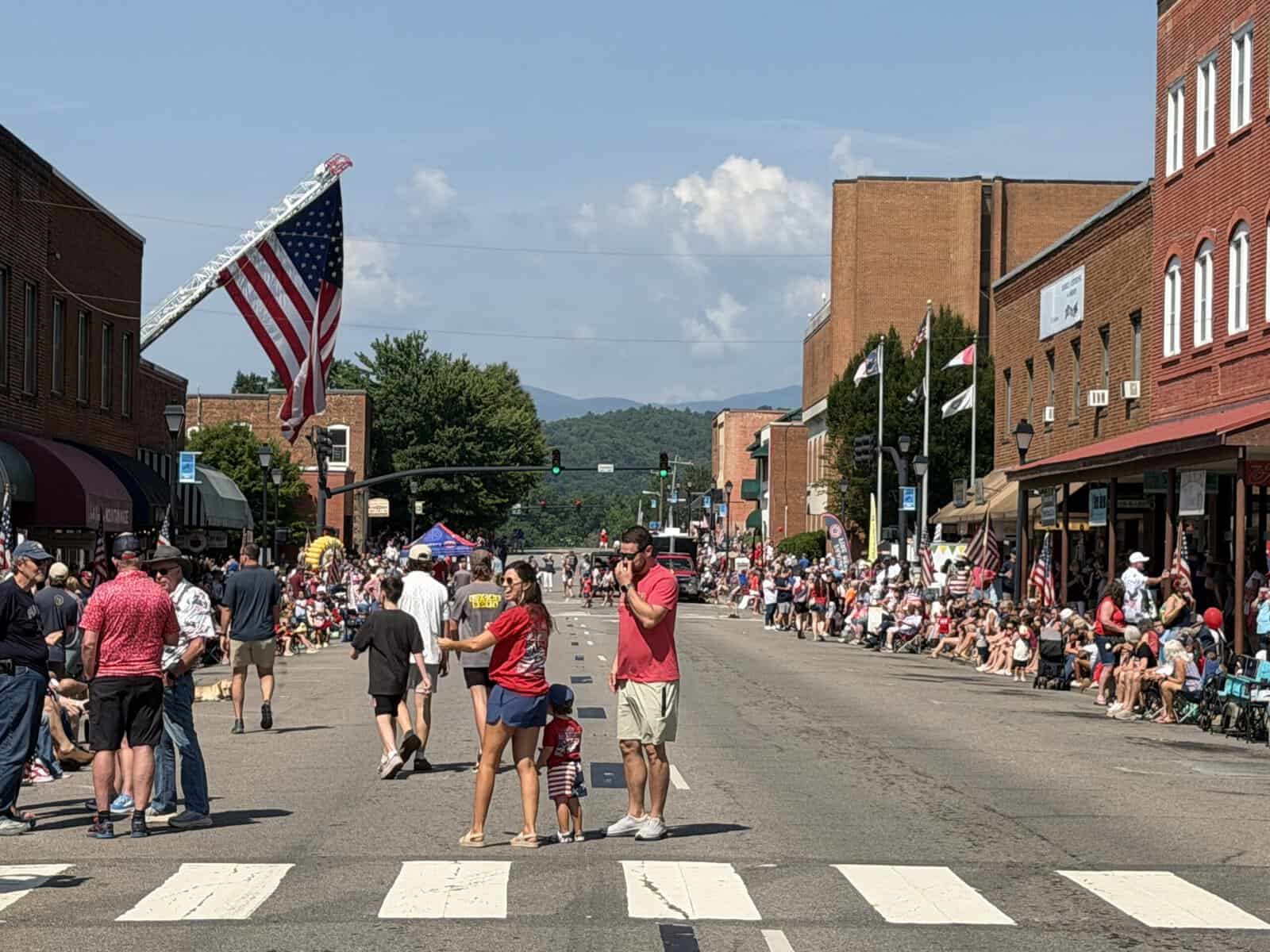 Crowd enjoying Macon County's America 250 parade with American flags and historic buildings.
