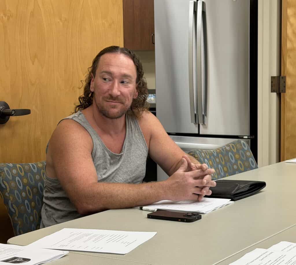 Man with long hair and beard sitting at table with documents and phone.