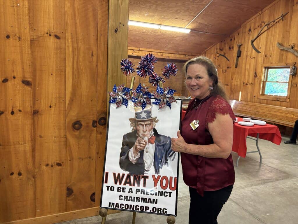 Woman standing next to campaign sign for precinct chairman in Macon County.