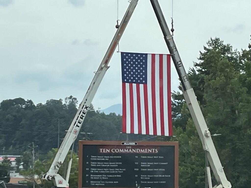 American flag being raised with cranes during Macon County event.