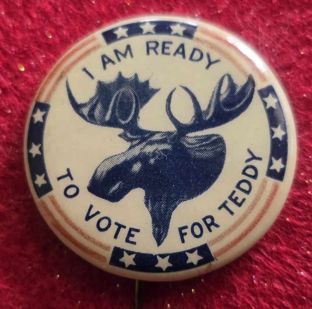 Vintage Teddy Roosevelt campaign button with moose illustration and patriotic design.