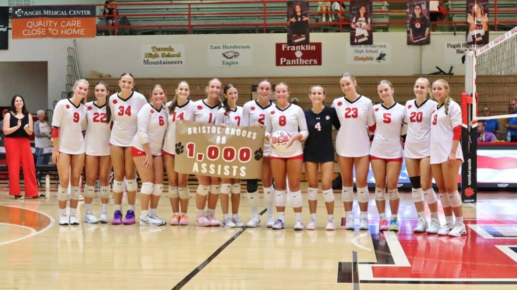 Girls volleyball team celebrating after reaching 1,000 assists in a match.