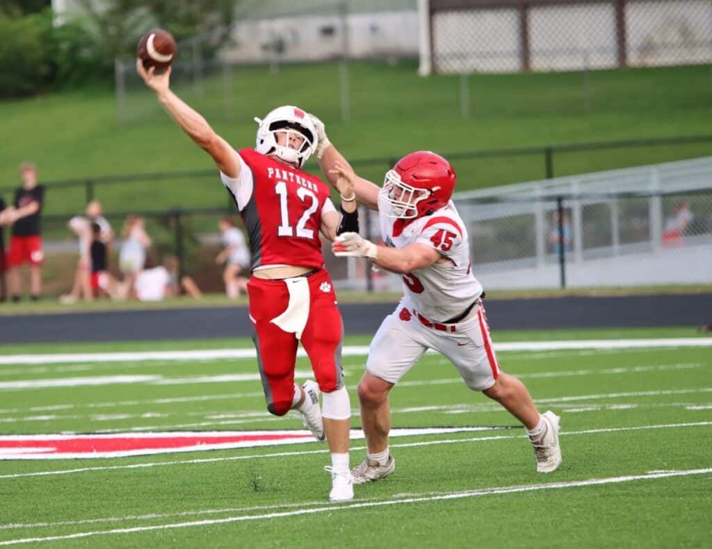 Panthers quarterback throws a pass while being tackled by a defender.