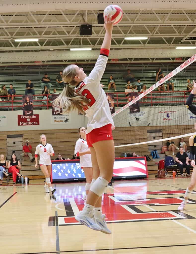 Female volleyball player jumping to serve during match at gymnasium.